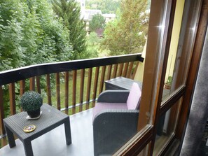 Ein Balkon mit einem kleinen Tisch, zwei Stühlen, einem Blumentopf und Blick auf ein Gebäude und Bäume.