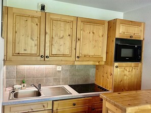 Une cuisine avec des meubles en bois, un évier en acier inoxydable, un micro-ondes noir et un plan de travail en granit.