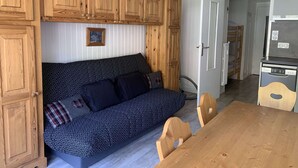 A compact living space with a sofa, wooden cabinets, a dining table, and a kitchenette. - Cozy studio cabin - 4 guests (Valloire)
