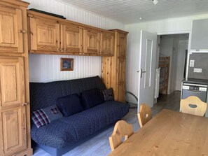 Ein kompakter Wohnbereich mit einer Couch, Holzschränken, einem Esstisch und einer Küchenzeile.