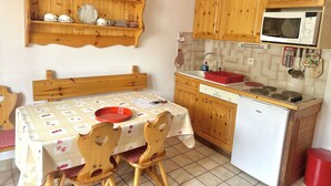 A compact kitchen with wooden cabinets, a microwave, a sink, and a dining area with a table and chairs. - Studio in the center - pets welcome - 4 guests (Valloire)