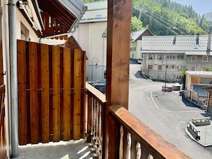 Un balcon doté d’une balustrade en bois, donnant sur un parking et des immeubles.