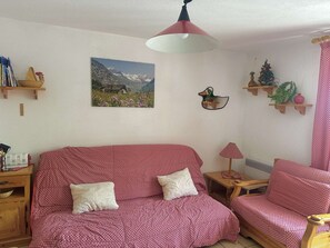 A cozy living room with a red patterned sofa, a wooden side table, a lamp, a wall-mounted duck decoration, and a framed mountain landscape picture. - Studio in the center - pets welcome - 4 guests (Valloire)