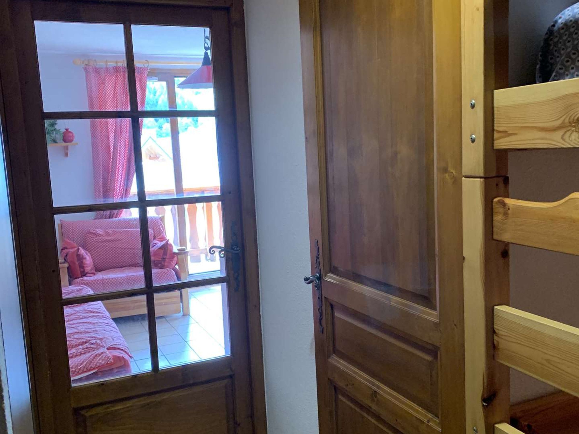 Une porte en bois avec un panneau de verre laissant entrevoir une pièce contenant un lit et des rideaux.