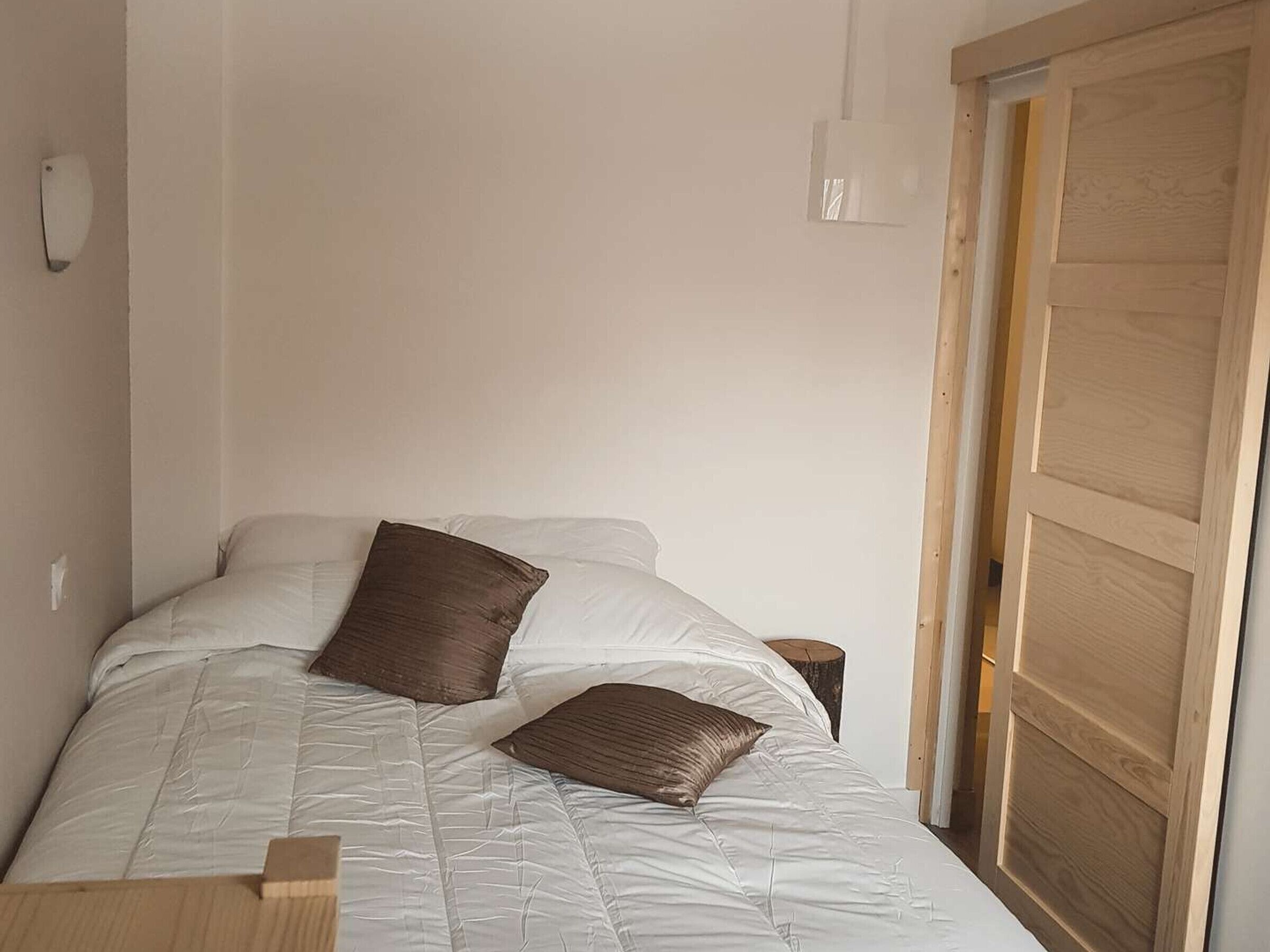 Un dormitorio con una cama, dos almohadas, una mesita de noche y una puerta de madera.