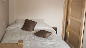 Een slaapkamer met een bed, twee kussens, een nachtkastje en een houten deur.