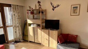 Een gezellige woonkamer met een houten tv-meubel, een boekenkast, een rode bank en een raam met gordijnen.