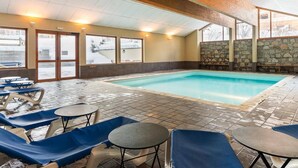 Une piscine intérieure dotée de chaises longues et de tables, de murs en pierre et de grandes fenêtres.