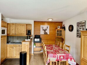 Een kleine keuken met houten kastjes, een magnetron, een koffiezetapparaat en een broodrooster. Er staat een eettafel met een rood-wit geruit tafelkleed, omringd door houten stoelen.