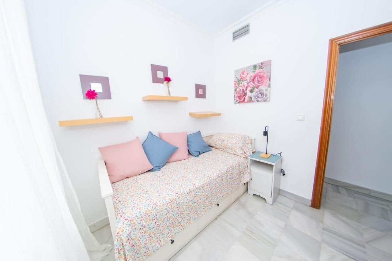 Un dormitorio con cama, mesita de noche y mesilla auxiliar. Hay repisas en la pared con objetos decorativos.