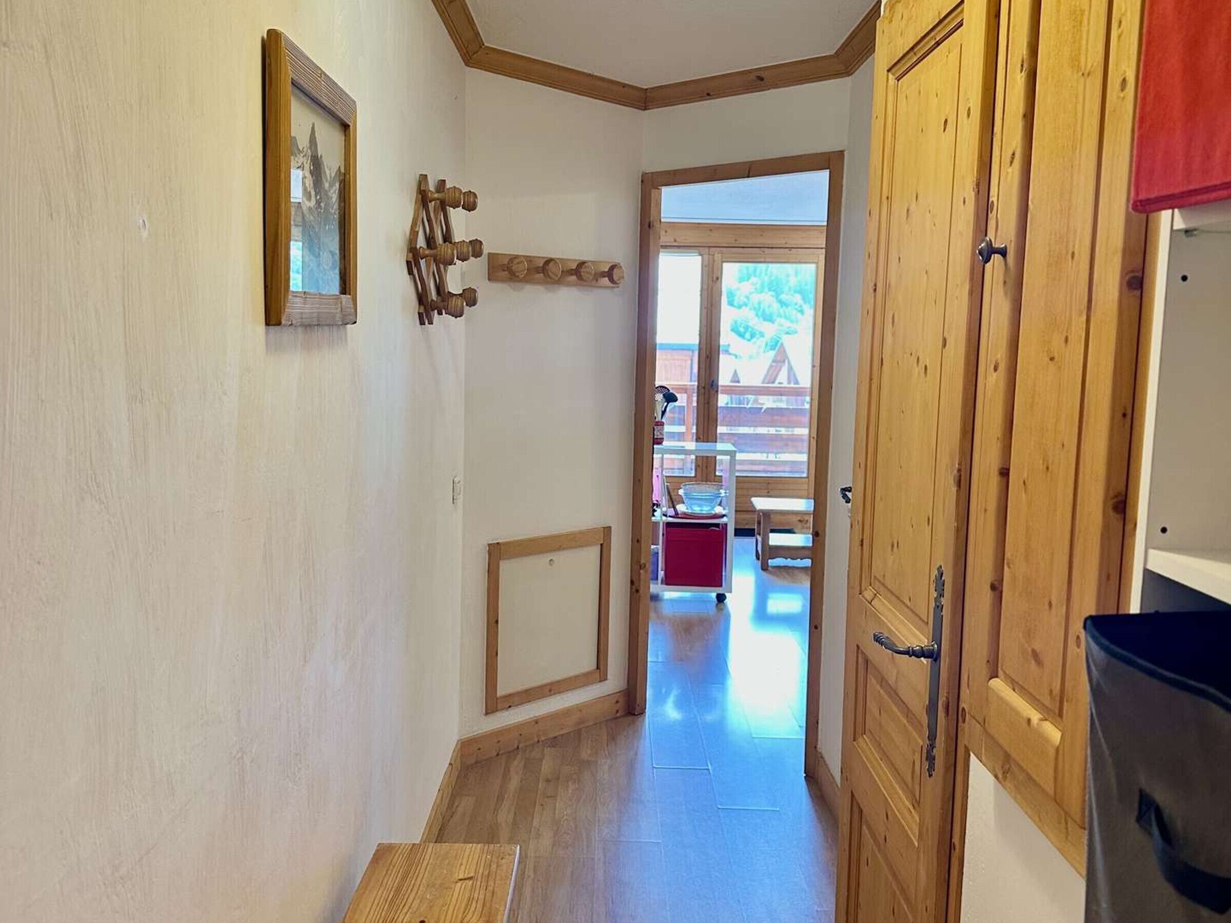 Un corridoio stretto con pareti e porta in legno. Si intravedono un tavolino e una sedia in lontananza, e una finestra in fondo al corridoio.