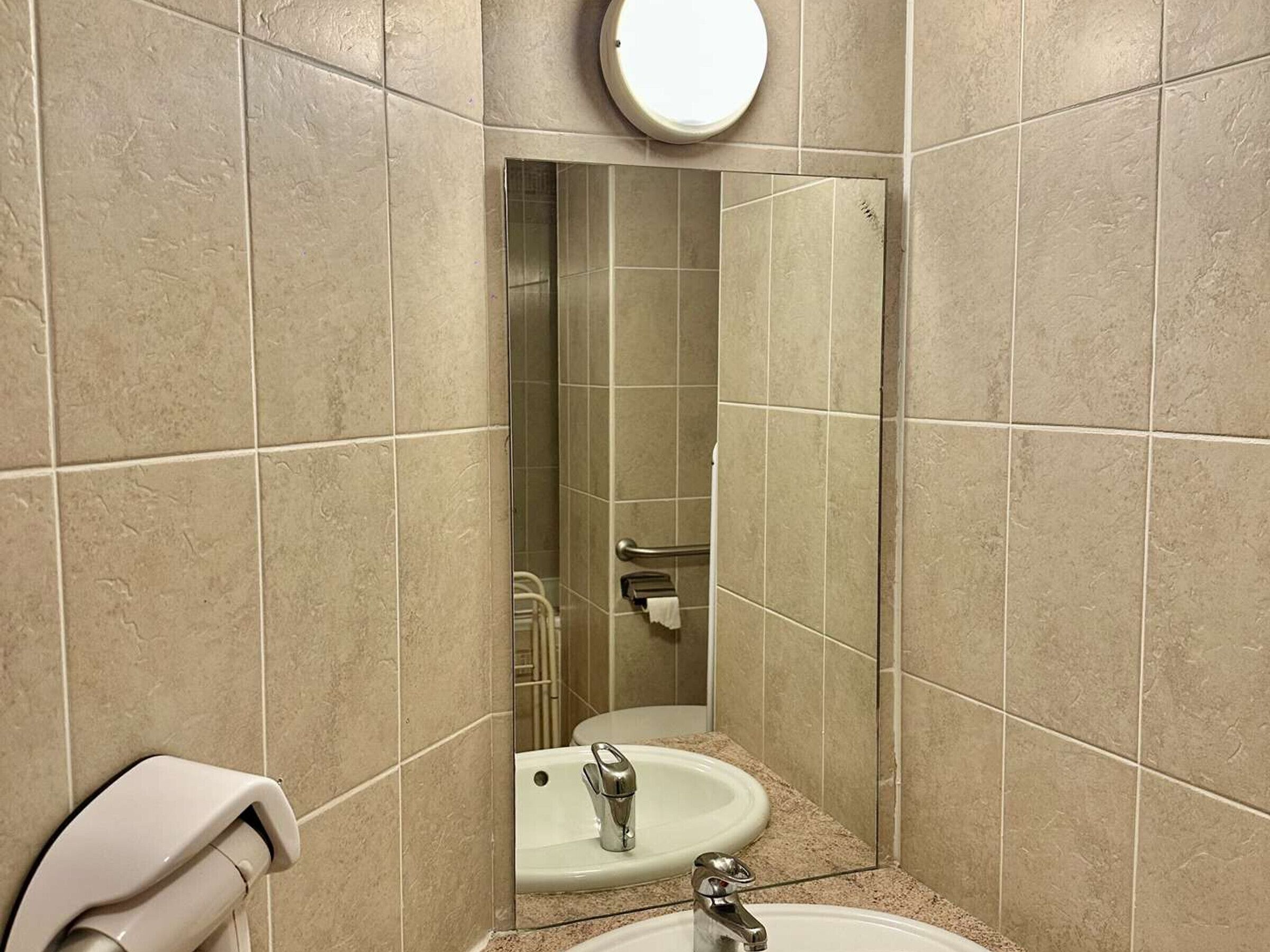 Une salle de bain avec des carreaux de couleur beige, un lavabo, un miroir et un sèche-mains.