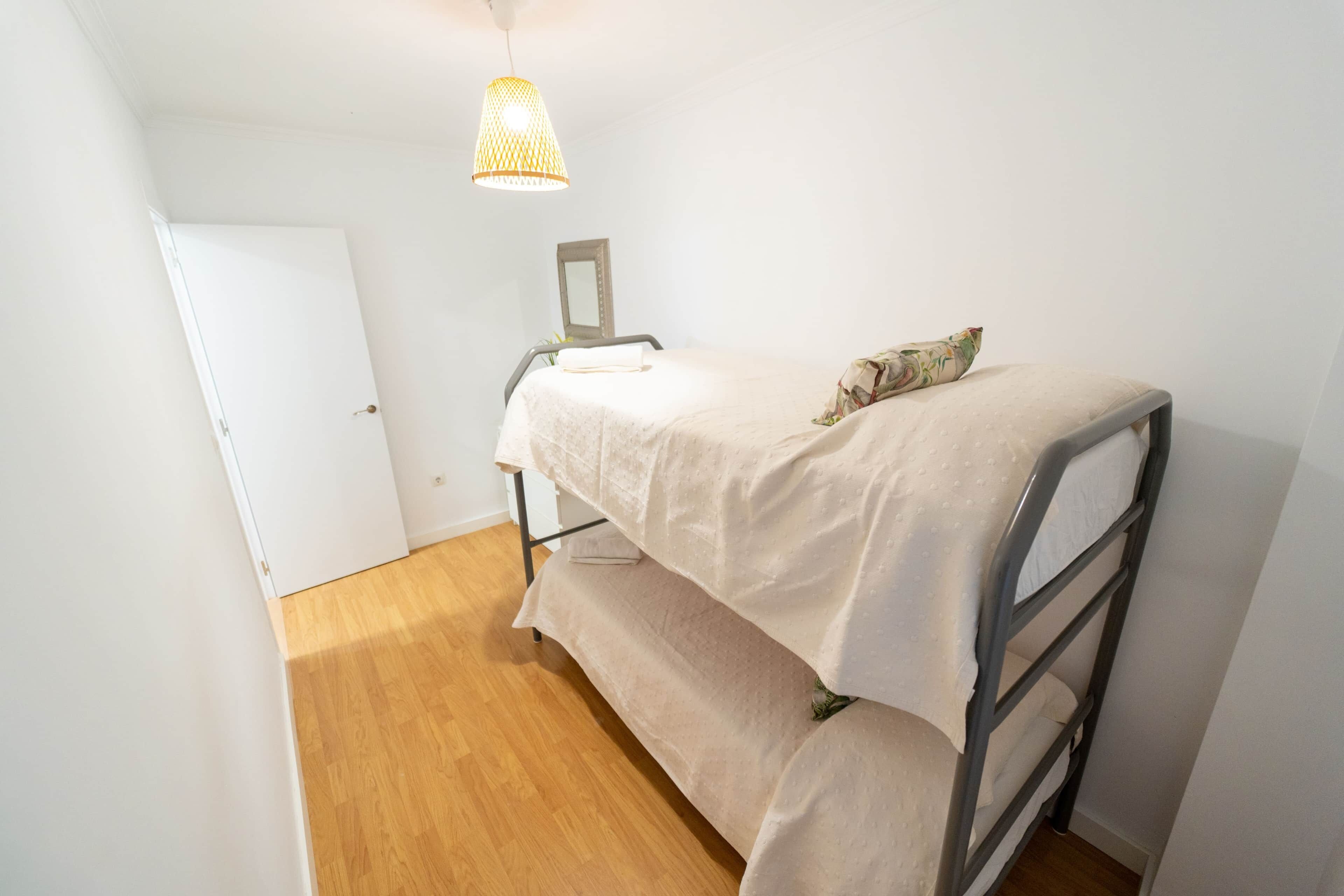 Una habitación pequeña con cama individual, piso de madera, puerta blanca y una lámpara colgante.