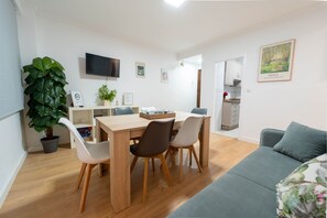 Ein modernes Wohnzimmer mit Essbereich, einem an der Wand montierten Flachbildfernseher und einer großen Topfpflanze.