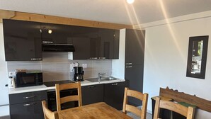 Kompakti keittiö, jossa on modernit kodinkoneet, ruokapöytä ja tuolit.