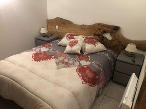 Een bed met een houten hoofdbord, twee nachtkastjes met lampen, en een bedsprei met dessin.