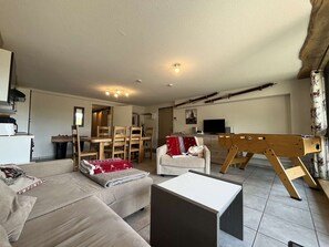 A living room with a sofa, a coffee table, a wooden easel, and a dining area with chairs and a table. - Comfortable apartment with parking - 6 guests (Valloire)