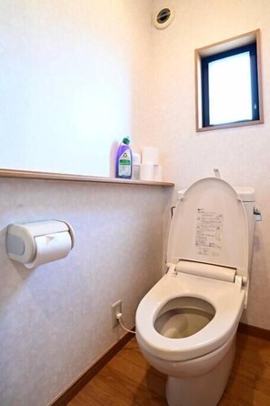 Une salle de bain standard équipée de toilettes, d’un distributeur d’essuie-tout et d’une fenêtre.
