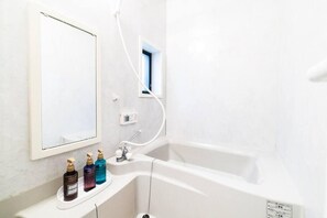 Une salle de bain avec une baignoire, un miroir et trois flacons de produits de toilette placés sur une étagère.