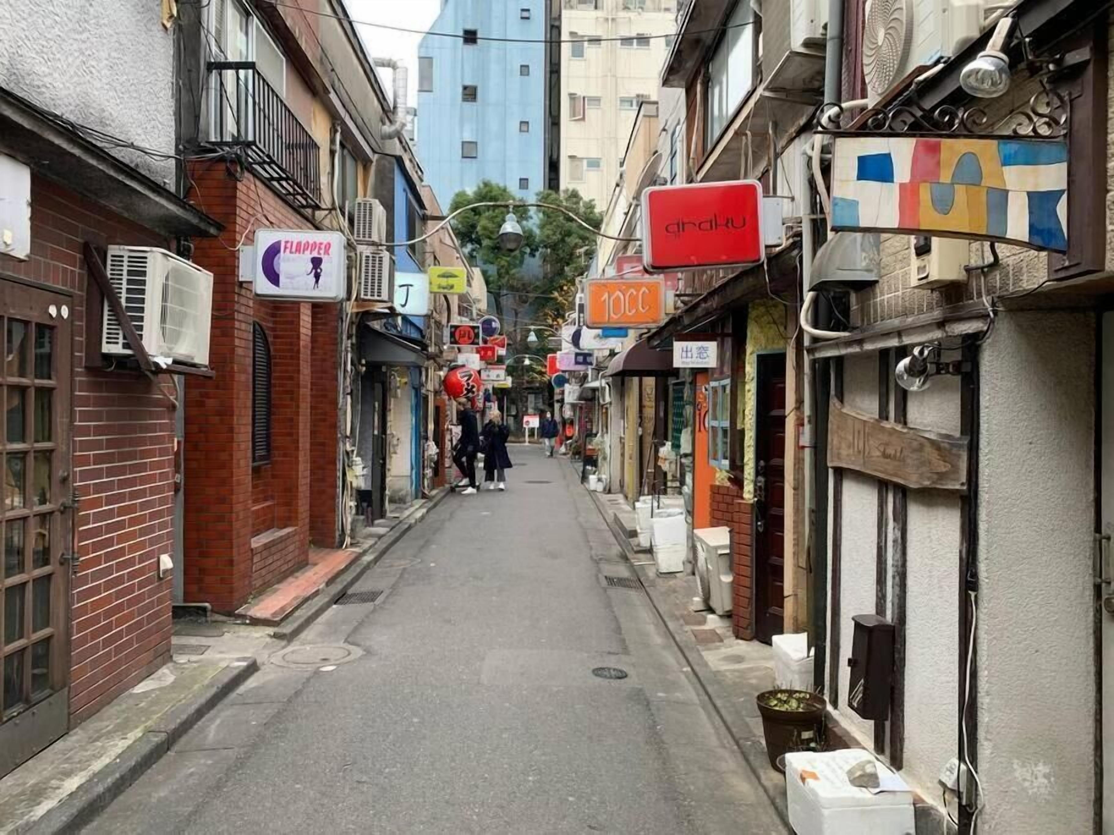 A narrow street lined with various shops and buildings, including a visible sign for 'Flapper' and another for '100C'.