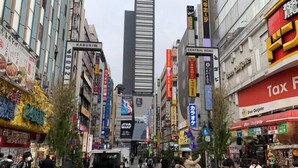 A busy urban street with various shops and signs, including a prominent 'Central Road' sign and a 'Tax' sign. - Honmachi 2 Chome (Tokyo)