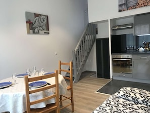 Ein Essbereich mit Tisch für zwei Personen, eine Treppe, die zu einer Küche führt, und ein Bett mit gemustertem Überwurf.