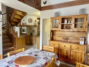 A cozy kitchen with wooden cabinets, a dining table with a patterned tablecloth, and a staircase leading to another room. - Triplex apartment, pets & parking - 10 guests (Valloire)