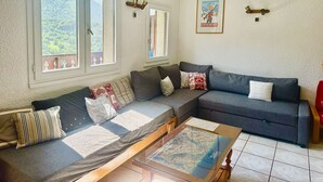 Olohuoneessa on sohva, sohvapöytä ja ikkuna, josta avautuu näkymä vehreään maisemaan.