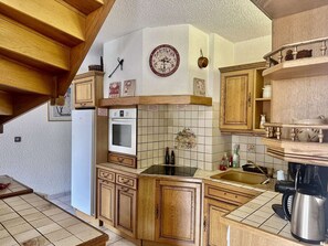 A kitchen with wooden cabinets, a built-in oven, a sink, and a clock on the wall. - Triplex apartment, pets & parking - 10 guests (Valloire)