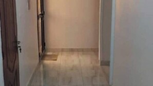 Un pasillo estrecho con una puerta de madera a la izquierda y una pared blanca a la derecha.