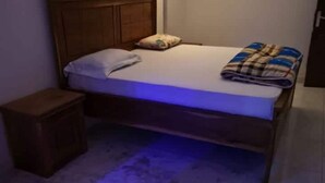 Una cama individual con cabecera de madera, una mesita de noche pequeña y una manta sobre la cama.