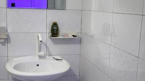 Baño con lavamanos blanco, dispensador de jabón y un portaceptos para cepillos de dientes en una pared de azulejos blancos.
