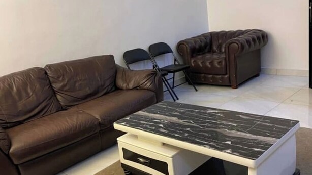 Un sofá de cuero marrón, una mesa de centro de mármol blanco y negro, y un sillón de cuero marrón en una habitación con paredes blancas y suelo de baldosas.