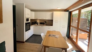 A compact kitchen with white cabinets, a dining table, and a large window. - Elegant apartment with parking - 6 guests (Valloire)