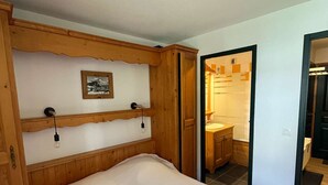 A bedroom with a wooden headboard, a bed, a nightstand, and a wall-mounted picture. - Elegant apartment with parking - 6 guests (Valloire)