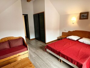 A room with a bed, a wooden bench, a red sofa, and a door. - Duplex apartment, parking - 6 guests (Valloire)