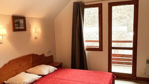 Ein Schlafzimmer mit einem hölzernen Bett, zwei Nachttischlampen, einem gerahmten Bild und einem Fenster mit Vorhängen.