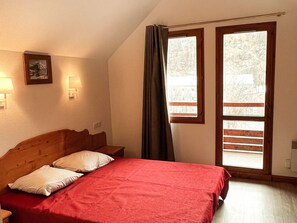 A bedroom with a wooden bed, two bedside lamps, a framed picture, and a window with curtains. - Duplex apartment, parking - 6 guests (Valloire)