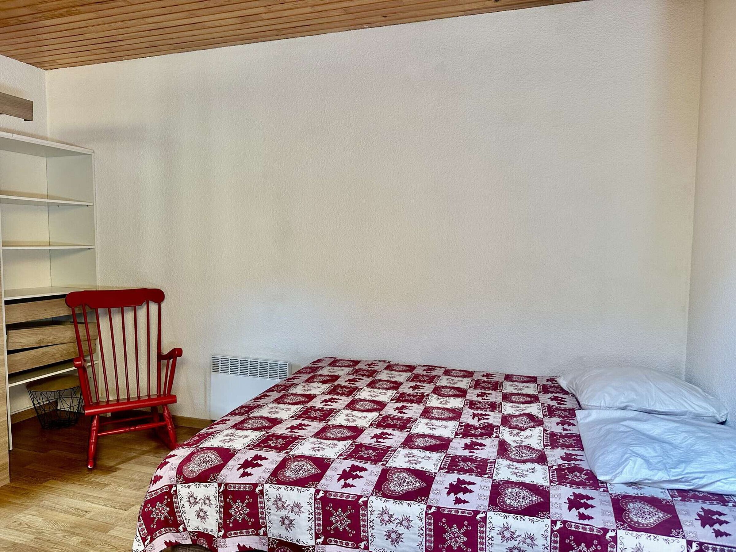 A bedroom with a bed, a red chair, and a white wall.