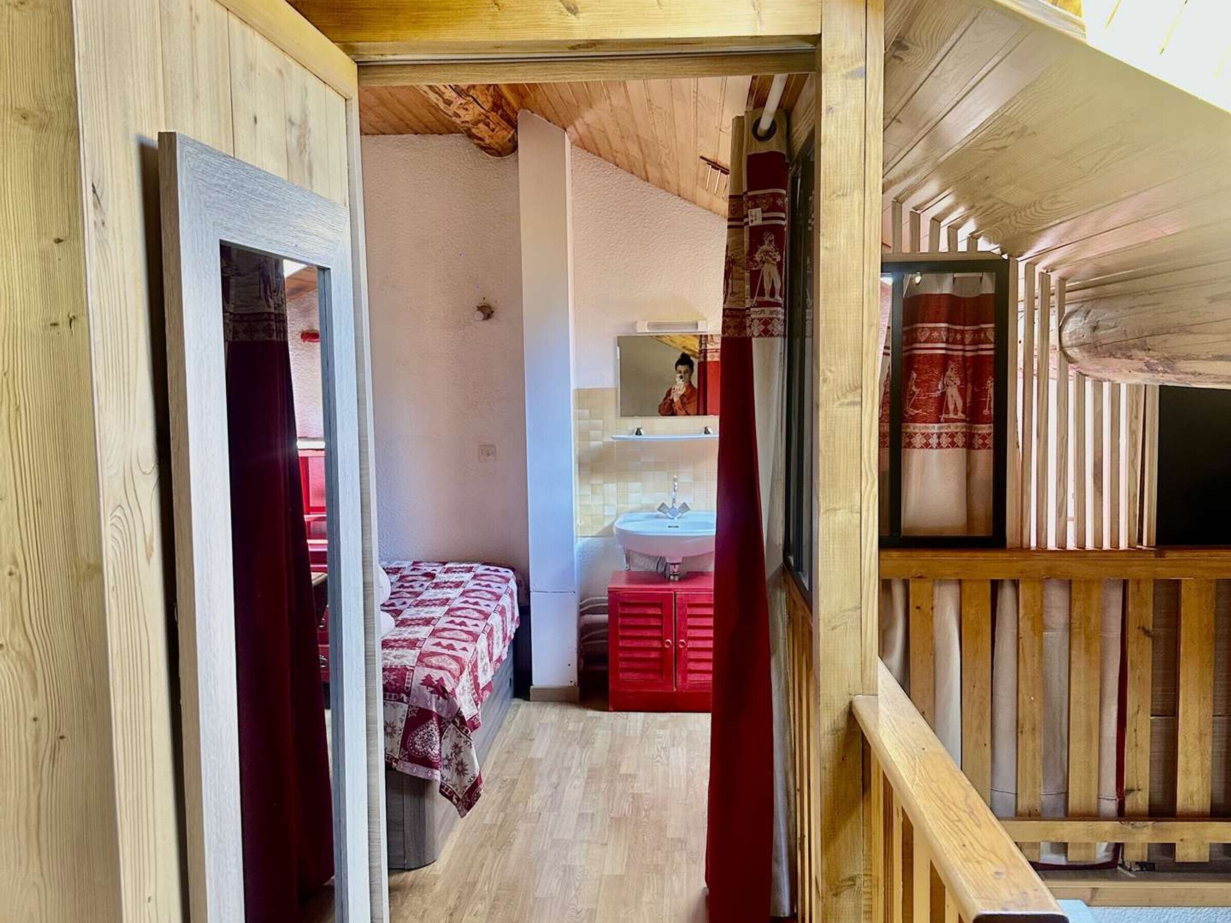 Un interno in legno con un letto, un armadio rosso e un lavandino bianco.