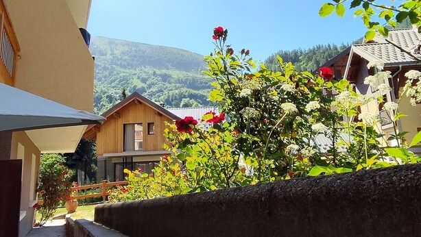 A wooden building with a balcony, surrounded by greenery and flowers.
