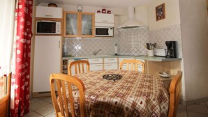 A compact kitchen with a dining table, chairs, a microwave, a coffee maker, and a tiled backsplash.