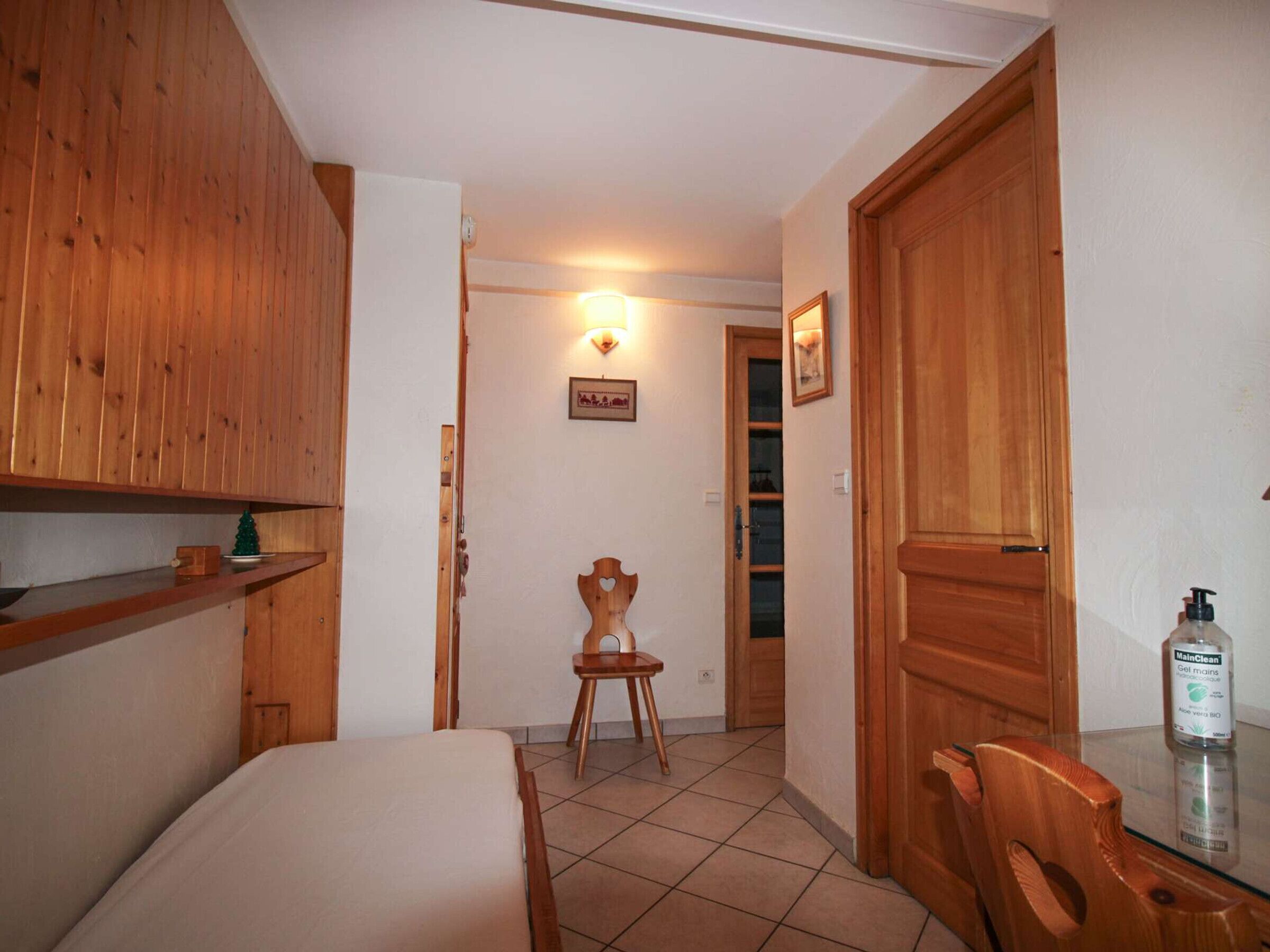A hotel room with wooden furniture, a bed, a small table, and a chair. There is a bottle of hand sanitizer on the table.