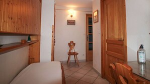 A hotel room with wooden furniture, a bed, a small table, and a chair. There is a bottle of hand sanitizer on the table.