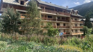 A multi-story hotel with balconies, a garden in the foreground, and a mountainous backdrop.