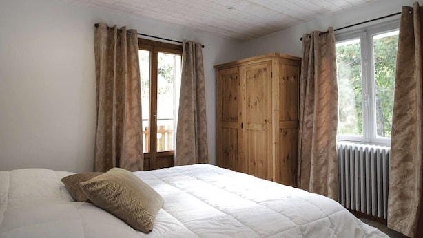 A bedroom with a bed, wooden wardrobe, and a window with curtains. - Central apartment, pets welcome - 6 guests (Valloire)