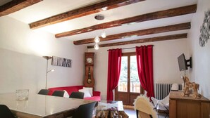 A dining area with a wooden table and chairs, a red sofa, a clock, and a wooden cabinet with a television. - Central apartment, pets welcome - 6 guests (Valloire)