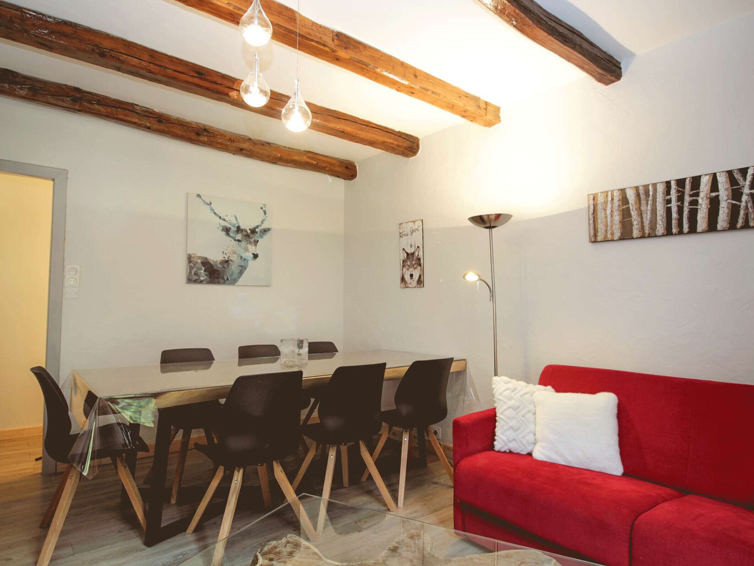 Un coin repas avec une table en bois, des chaises noires et un canapé rouge.