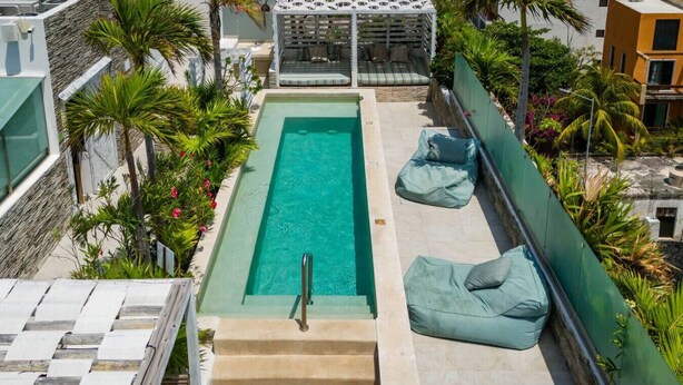 Una piscina sul tetto con vista libera sul cielo, circondata da palme e un'area lounge coperta.