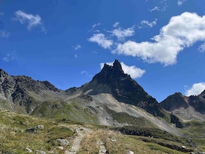 Eine gebirgige Landschaft mit einem markanten Gipfel, blauem Himmel und einem Weg, der zum Gipfel hinaufführt.